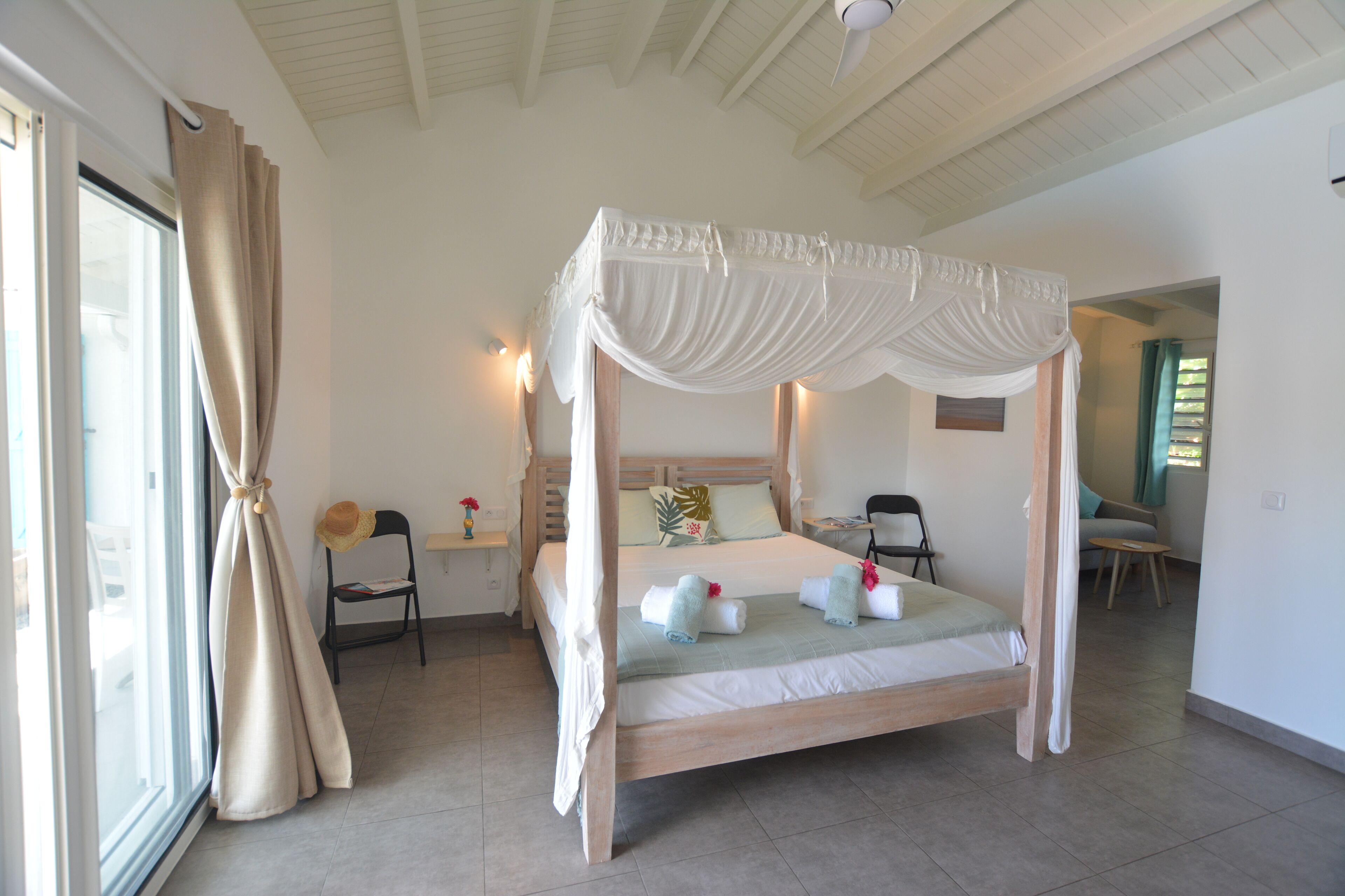 A four-poster bed with a canopy, a chair, a small table, and a view of the outside.