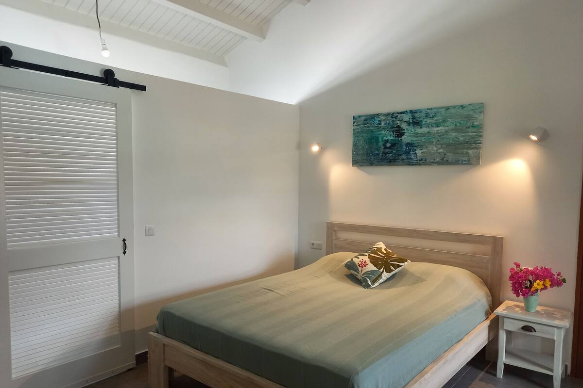 Ein Schlafzimmer mit einem Bett, einem Nachttisch, einer Wandleuchte und einem Deckenventilator.