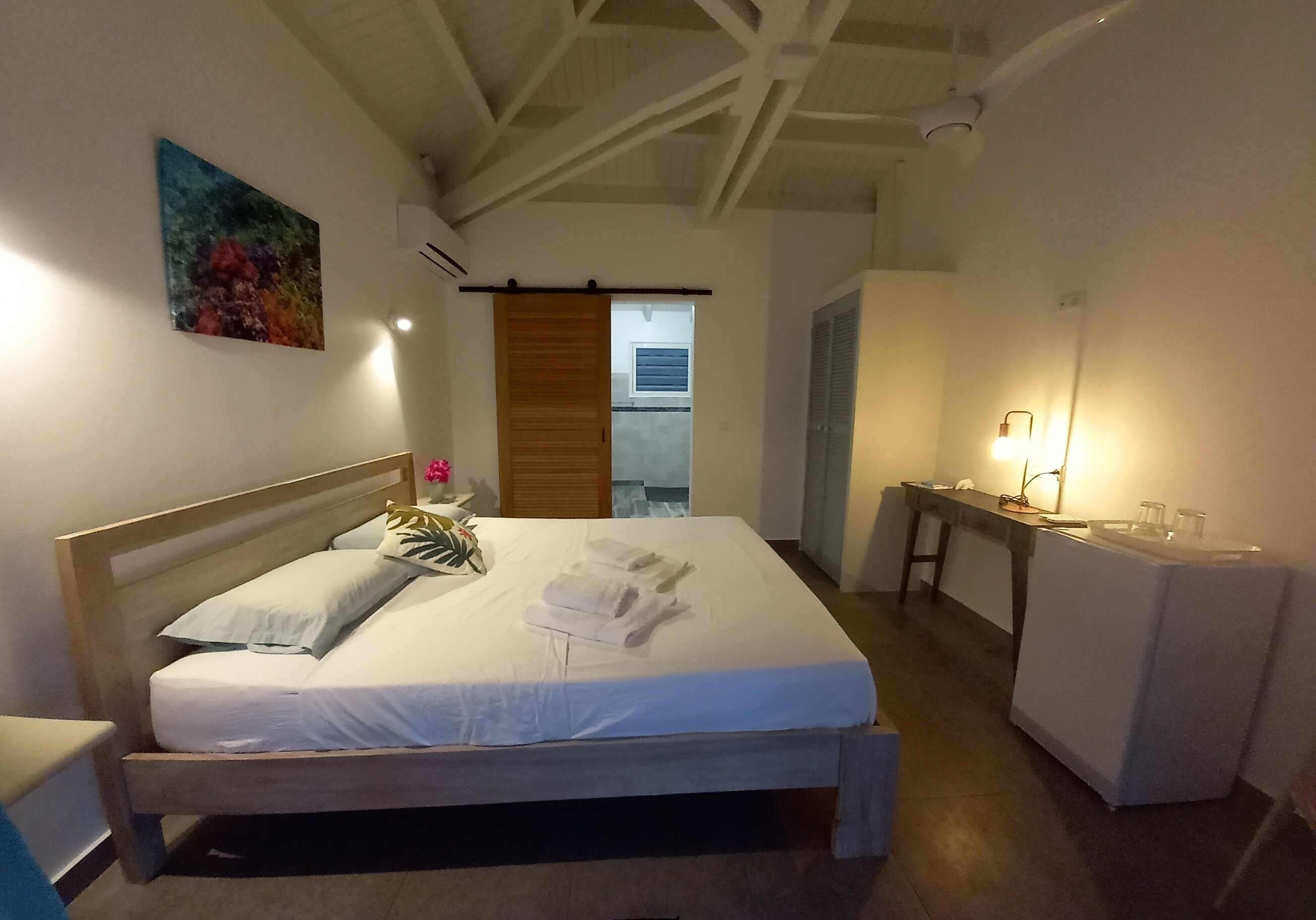Un dormitorio con una cama de madera, una mesita de noche con lámpara y un cuadro en la pared.