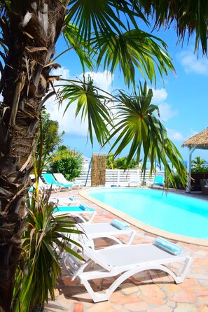 A pool area with lounge chairs and palm trees. - Tiko lodge sxm (Oyster Pond)
