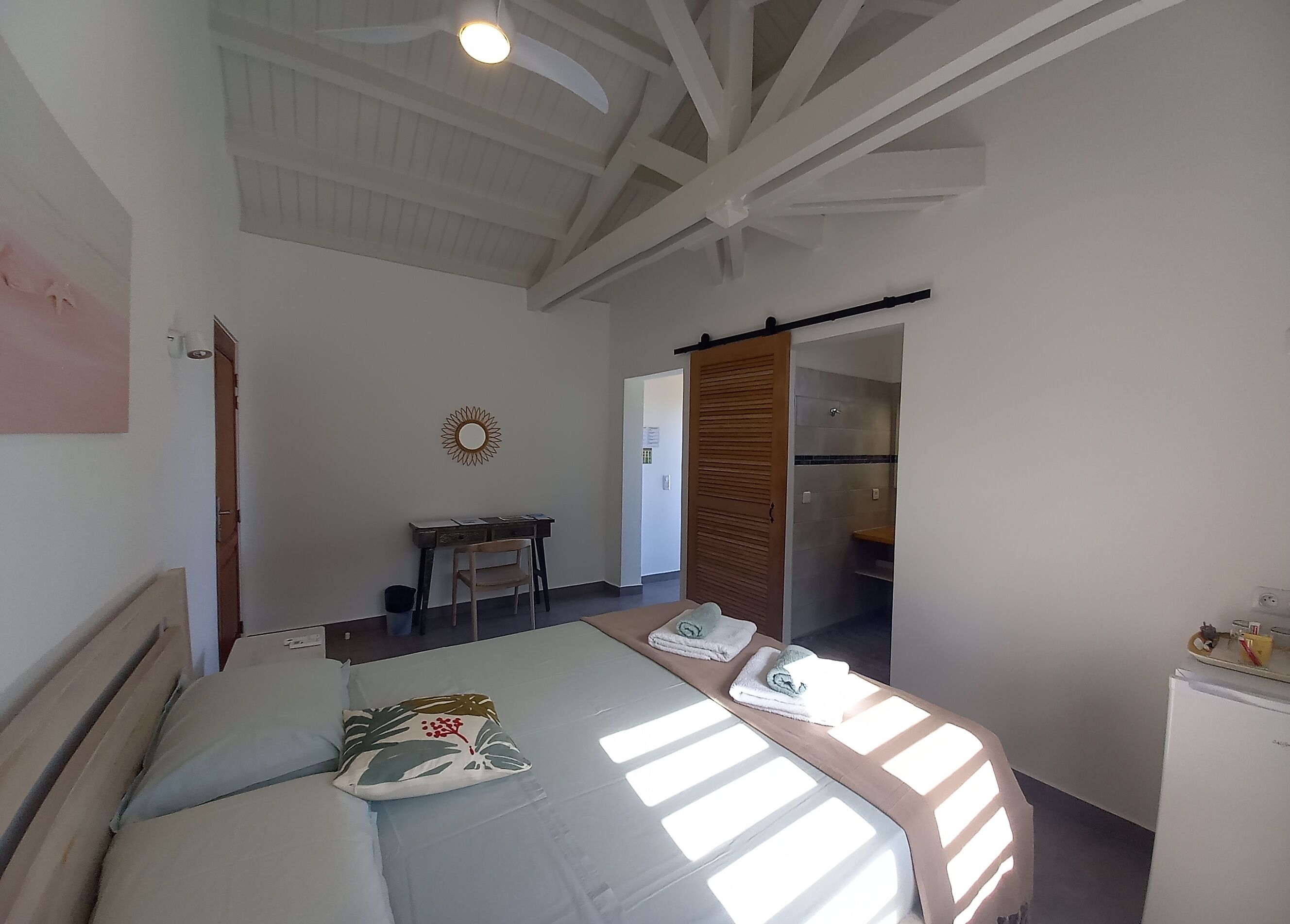 Un dormitorio con cama, escritorio, silla, armario y baño visible a través de una puerta abierta.