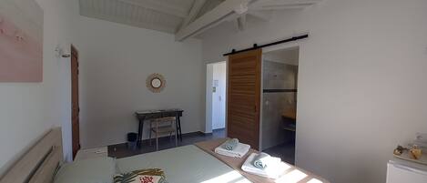 Un dormitorio con cama, escritorio, silla, armario y baño visible a través de una puerta abierta.