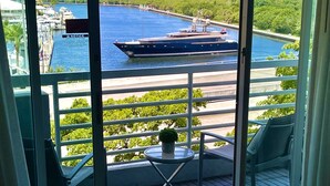A balcony with a view of a marina, a large boat, and a distant building. - Apart Suites By Hilton. Top View. (Fort Lauderdale)