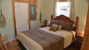 A bedroom with a wooden bed, a nightstand with a lamp, a chair, and a door. - The Hiwassee Cabin at Starr Mountain Retreat (Reliance)