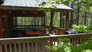 A wooden deck with outdoor seating, a grill, and a view of a forested area. - The Hiwassee Cabin at Starr Mountain Retreat (Reliance)