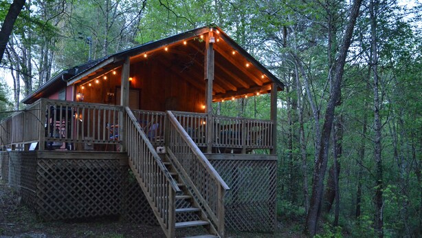 A wooden cabin with a deck and stairs, surrounded by trees. - The Hiwassee Cabin at Starr Mountain Retreat (Reliance)