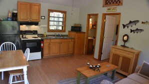 A compact kitchen with wooden cabinets, a dining table, and a small seating area. - The Hiwassee Cabin at Starr Mountain Retreat (Reliance)