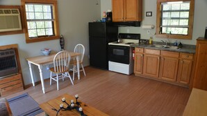 A compact kitchen with wooden cabinets, a black refrigerator, a stove, and a sink. There is a dining table with two chairs and a small wooden table with candles. - The Hiwassee Cabin at Starr Mountain Retreat (Reliance)