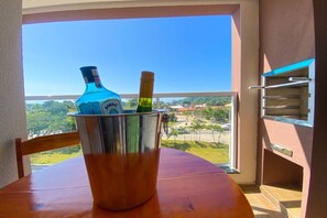A balcony with a view of a coastal landscape, a metal bucket containing a bottle and a bottle of Bombay Sapphire gin, and a wooden chair. - BEAUTIFUL APARTMENT 26 - with sea view, two parking spaces, we have other options. (Ubatuba)