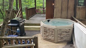 Una terraza de madera con un jacuzzi, una parrilla y mobiliario para exteriores.