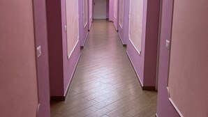 A long, narrow hallway with pink walls and wooden flooring.