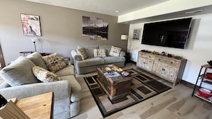 Un salon avec un canapé gris, une table basse et un téléviseur fixé au mur.