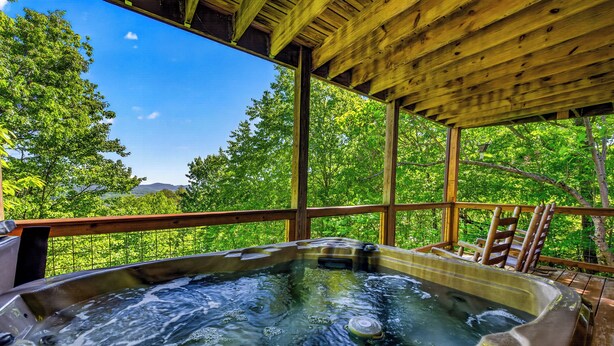A hot tub with a wooden deck and a view of lush greenery.