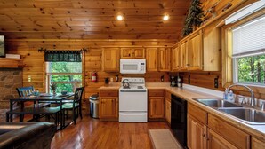 A wooden cabin interior with a kitchen, dining area, and a fireplace.