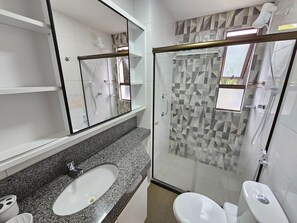 Un baño con cabina de ducha de vidrio, un lavabo con encimera de granito y un inodoro.