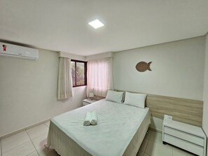 Ein Schlafzimmer mit Bett, Nachttisch, Wand-Klimaanlage, Fenster mit Vorhängen und Wanddeko.