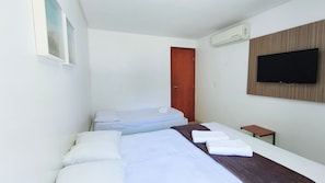 A hotel room with two beds, a TV, an air conditioner, and a wooden panel wall. - Carneiros Beach Resort - Praia Carneiros (Tamandaré)