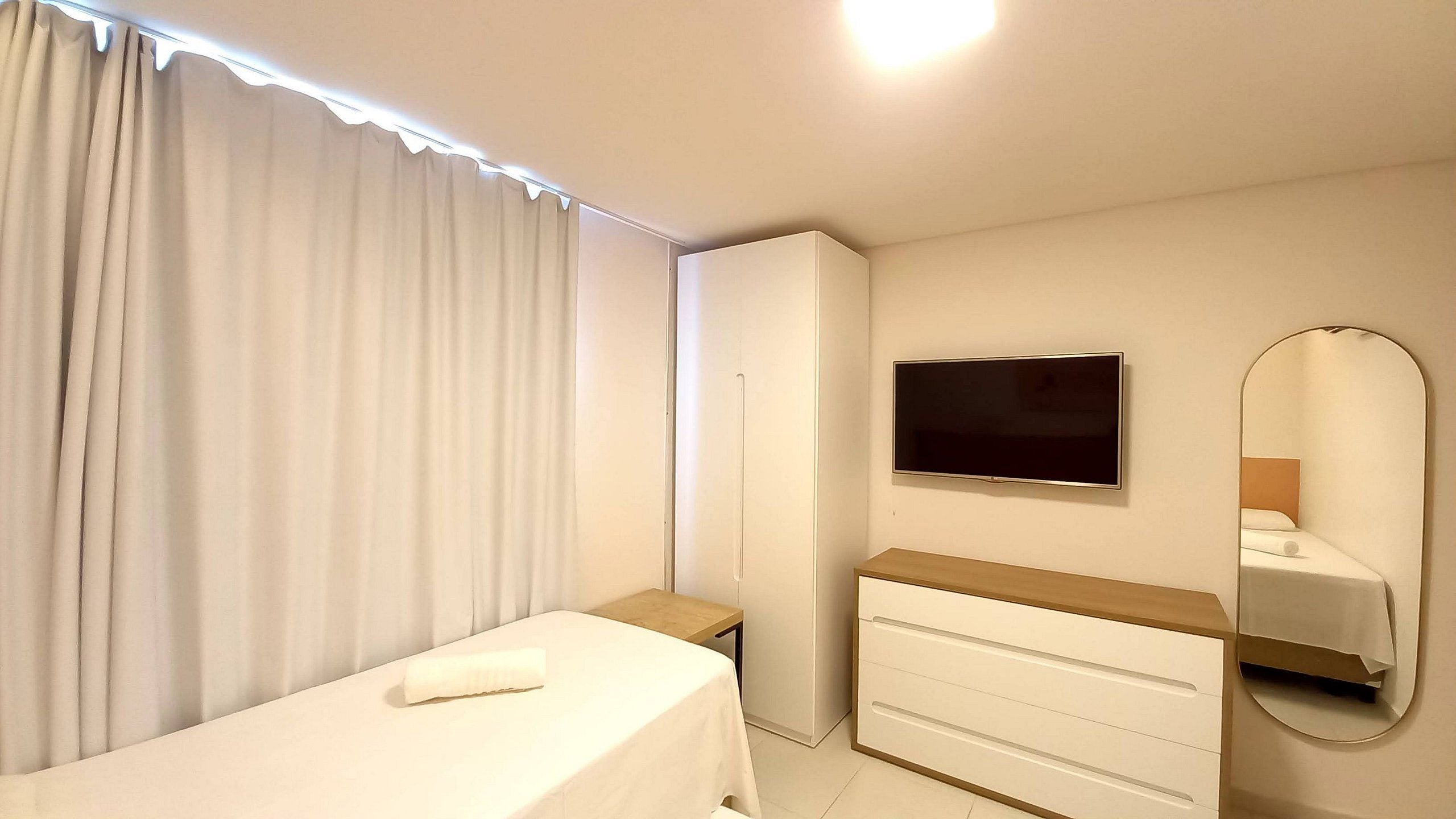 A bedroom with a bed, a dresser, a television, and a mirror.