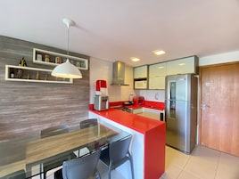Una cocina moderna con una isla roja, electrodomésticos de acero inoxidable y una mesa de comedor de vidrio.
