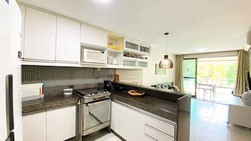 A modern kitchen with white cabinets, a microwave, a stove, and a dining area with a view.