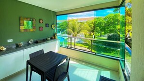 A balcony with a view of a pool and greenery, a dining table with chairs, and decorative items on the counter. - Carneiros Beach Resort - Praia Carneiros (Tamandaré)