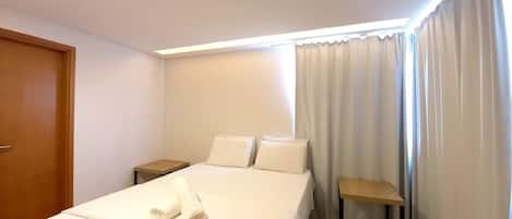 A hotel room with a bed, two pillows, a wooden nightstand, a small table, and a door.