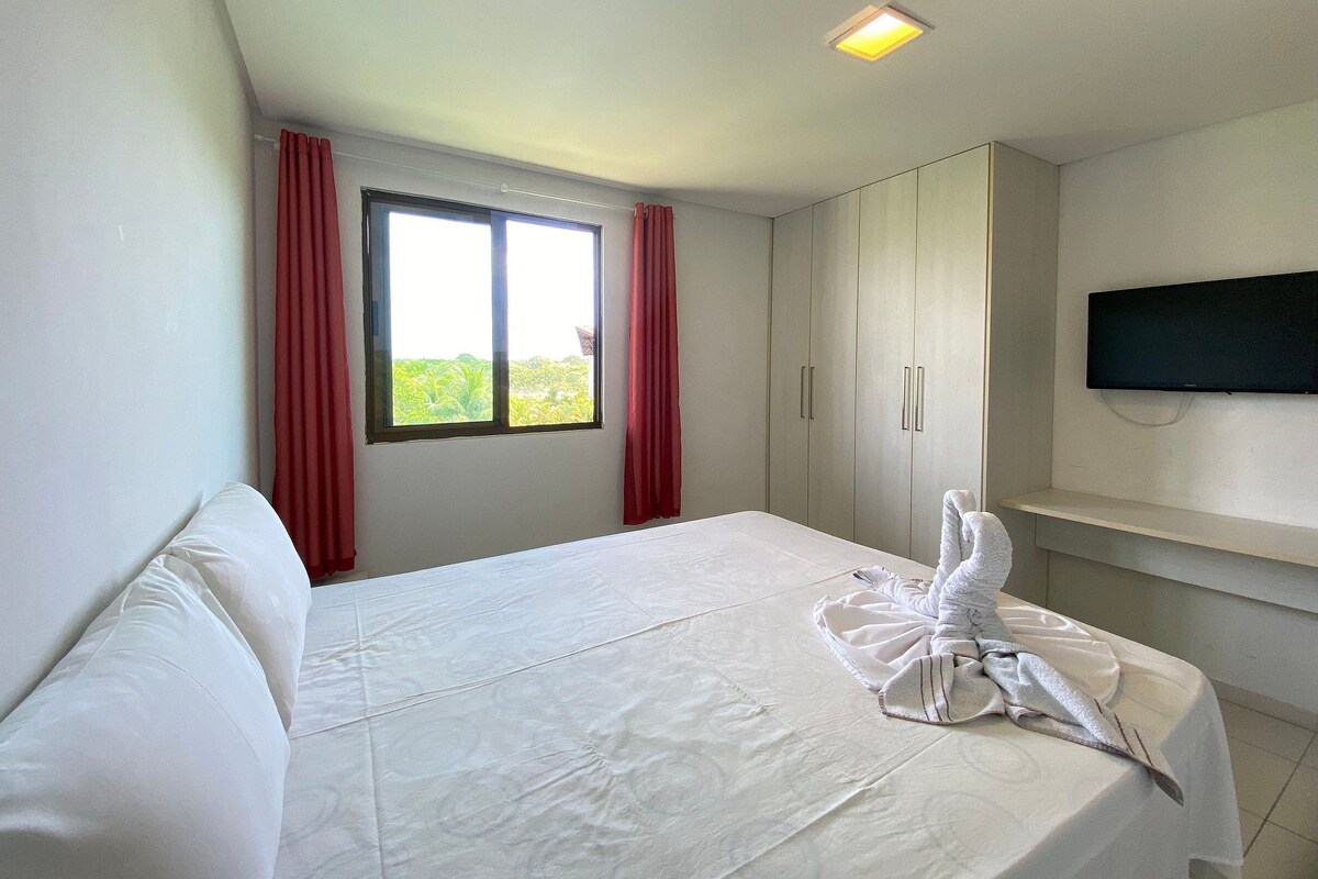Una habitación de hotel con una cama, un televisor montado en la pared y una ventana con cortinas.