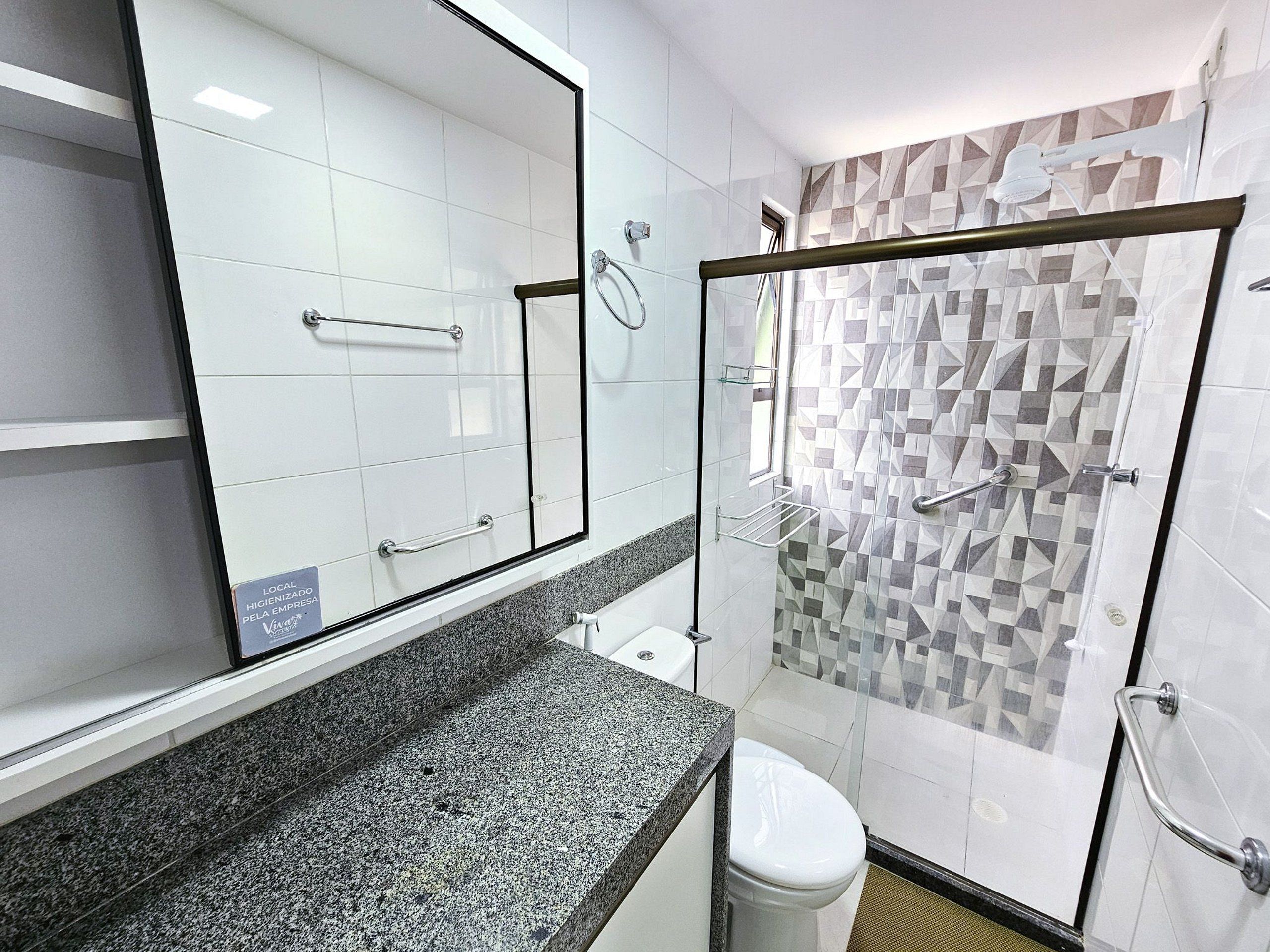 Ein modernes Badezimmer mit einer Duschkabine aus Glas, einer Arbeitsplatte aus Granit, einer weißen Toilette und einem Spiegel mit der Aufschrift 'LOCAL HIGIENIZADO'.