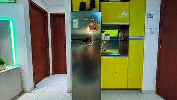 Cozinha com geladeira de aço inoxidável, armário amarelo e parede iluminada em verde.