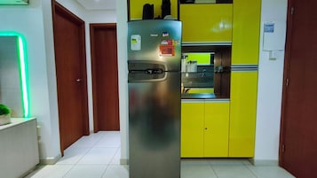 Una cocina con un refrigerador de acero inoxidable, un mueble amarillo y una pared iluminada en verde.
