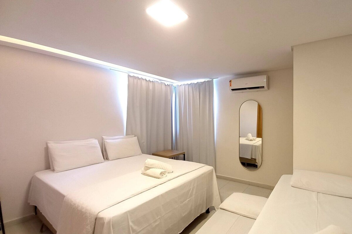 Una habitación de hotel con una cama grande, una cama más pequeña, una mesita de noche, un espejo y un equipo de aire acondicionado.