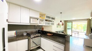 A modern kitchen with white cabinets, a microwave, a stove, and a dining area with a view. - Carneiros Beach Resort - Praia Carneiros (Tamandaré)