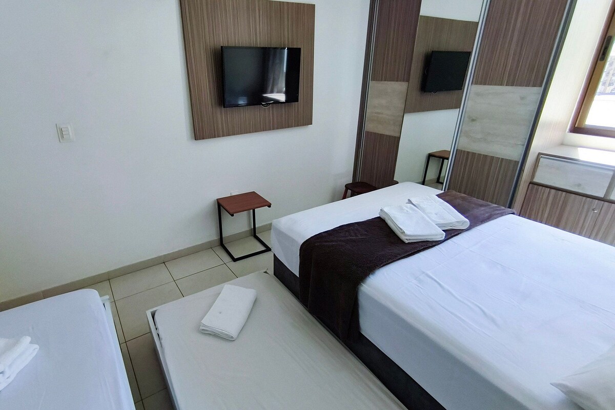Habitación de hotel con dos camas, un televisor montado en la pared, una mesita y un espejo.