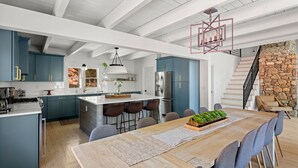 Une cuisine moderne avec des meubles bleus, un îlot central en bois et un coin repas comprenant une longue table et des chaises.