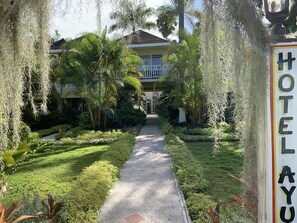 A pathway leading to a hotel entrance with lush greenery and a sign reading "HOTEL AYYU".