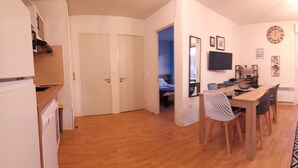 A compact living space with a kitchenette, a dining area, and a seating area with a sofa and a patterned rug. - Appartement de L'isard Bleu, Dans Résidence de Tourisme 3 Étoiles (Lourdes)
