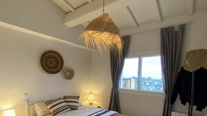 Un dormitori amb un llit, làmpades de sobretaula, llum penjant, una finestra amb cortines i vista a la ciutat.