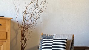 Una cadira de fusta amb un coixí estriat, una planta en test i dibuixos botànics emmarcats a la paret.