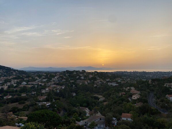 A coastal town at sunset with a view of the sea and distant mountains.