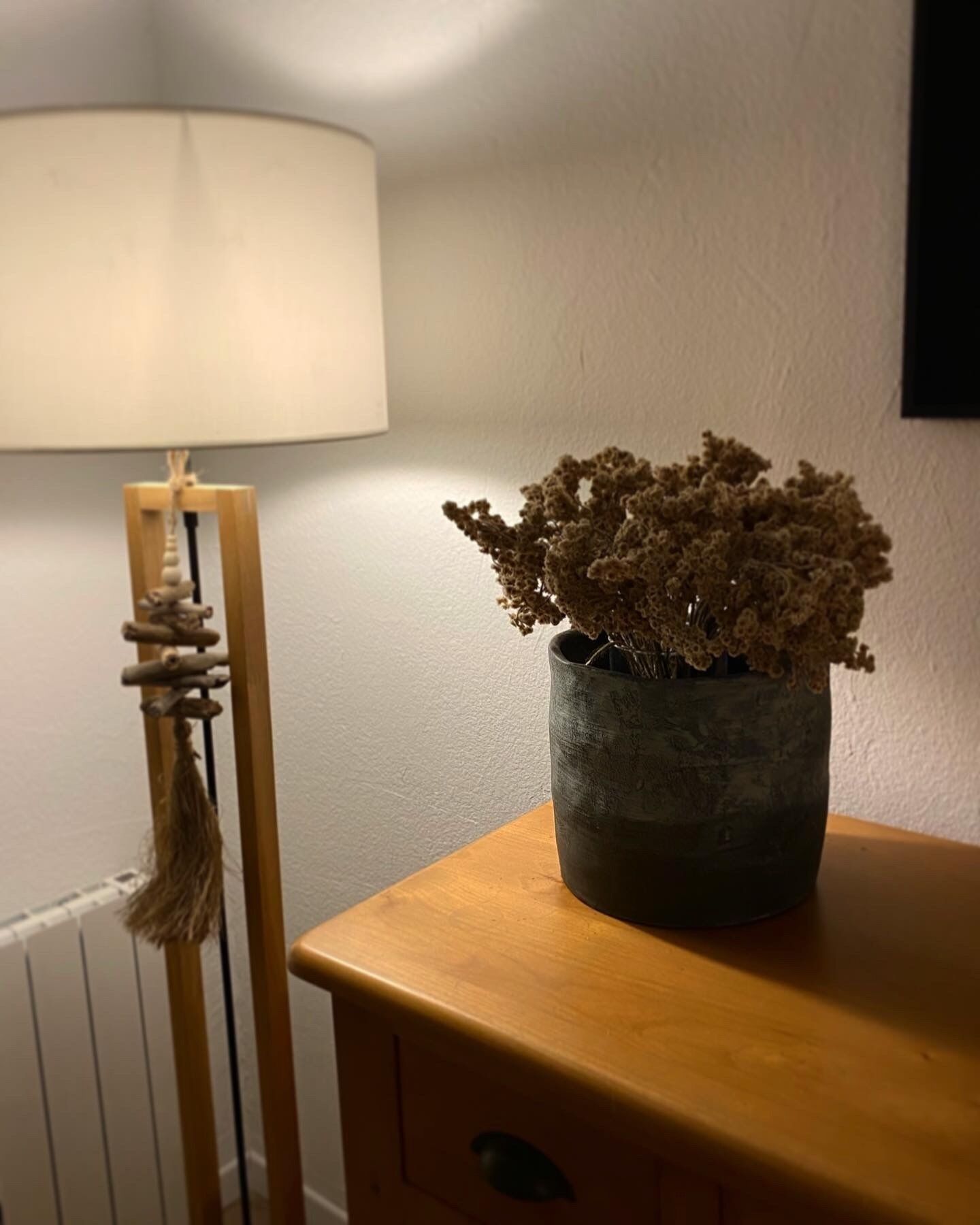 A wooden bedside table with a potted plant and a lamp.