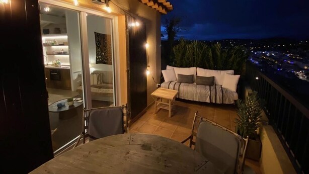 Un balcó amb un sofà i cadires, una taula de dinar i vista a la ciutat de nit.