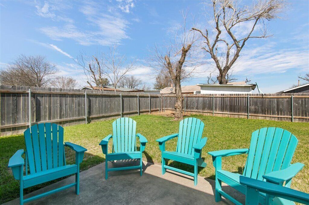 A backyard with four turquoise Adirondack chairs arranged on a concrete patio.