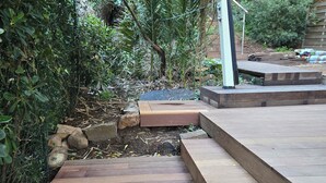 A wooden pathway leading through a garden with dense foliage and a metal structure in the background. - Authentic waterfront villa (1st line) with private beach access (Saint Raphael)