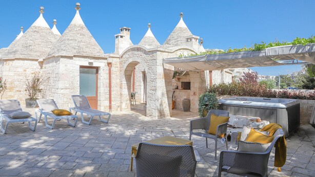 A stone building with conical roofs, outdoor seating with cushions, and a hot tub.