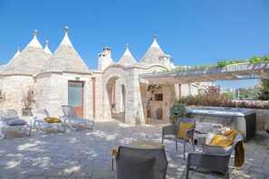A stone building with conical roofs, outdoor seating with cushions, and a hot tub. - TRULLI CALELLA - QUERCIA by Apulia Hospitality (Locorotondo)