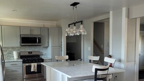 Una cocina moderna con una isla central, electrodomésticos de acero inoxidable y una lámpara colgante.