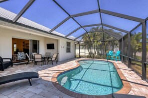 A covered outdoor swimming pool with a patio area, seating, and a view of palm trees.