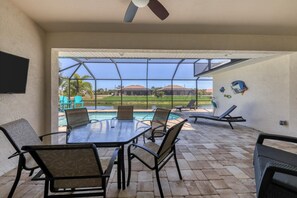 A covered outdoor area with a pool, lounge chairs, and a table with chairs.