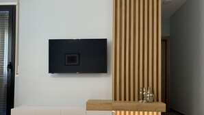 A modern living room with a flat-screen TV mounted on a white wall, a wooden slatted partition, and a built-in bench with decorative vases.