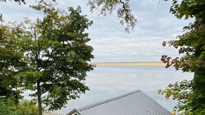 A small wooden cabin with a metal roof, surrounded by lush greenery and overlooking a calm body of water. - NEW Dock with large platform.  Bring the boat!  Lakefront Farmhouse.   (Romulus)